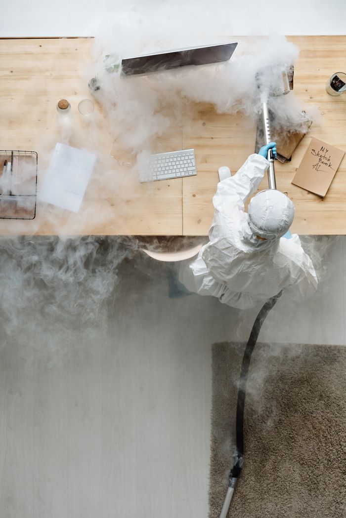 who-we-are A person in protective gear sanitizing an office desk using fumigation equipment during daytime.